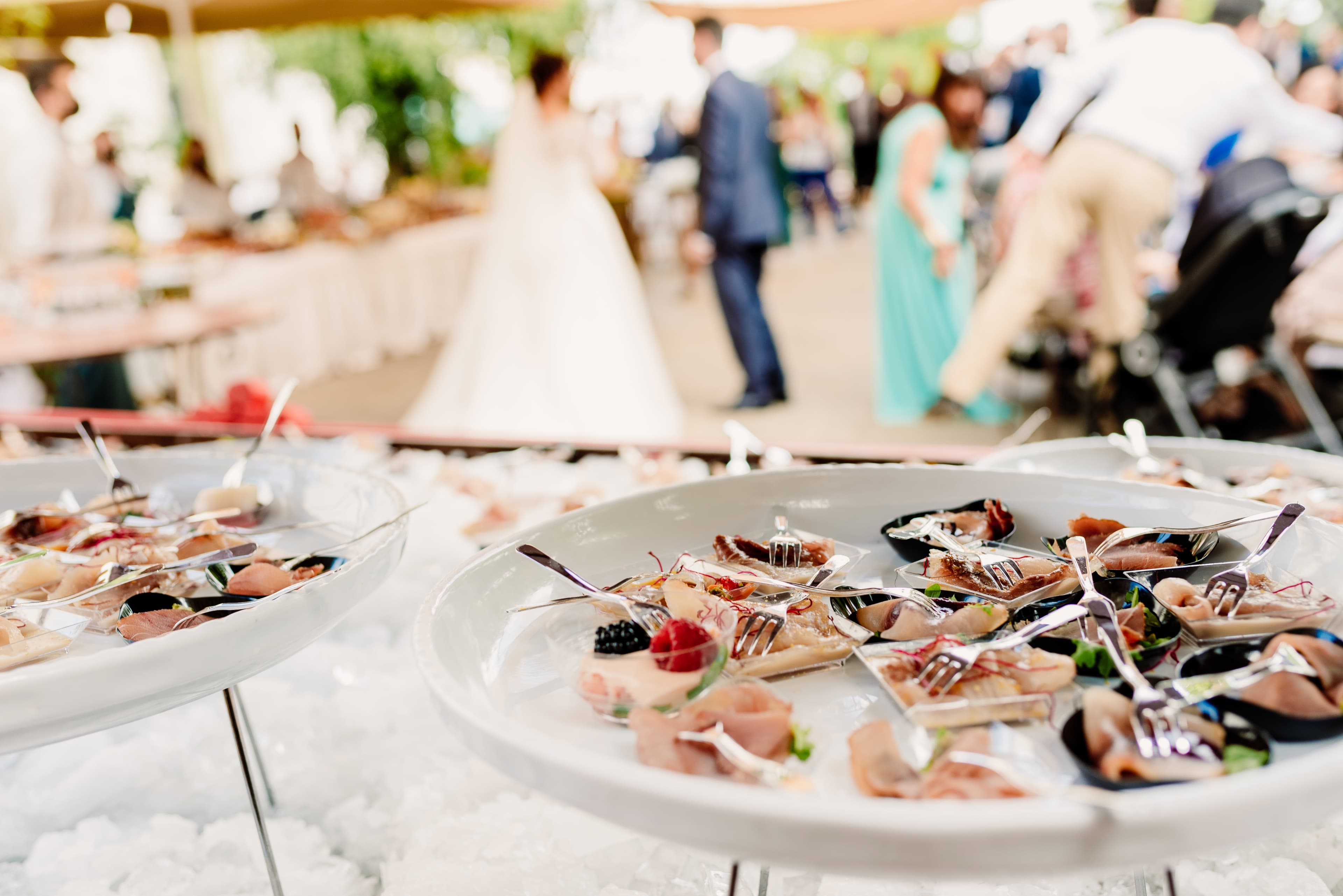 Aperitivos fríos servidos sobre hielo en una boda, con los novios al fondo