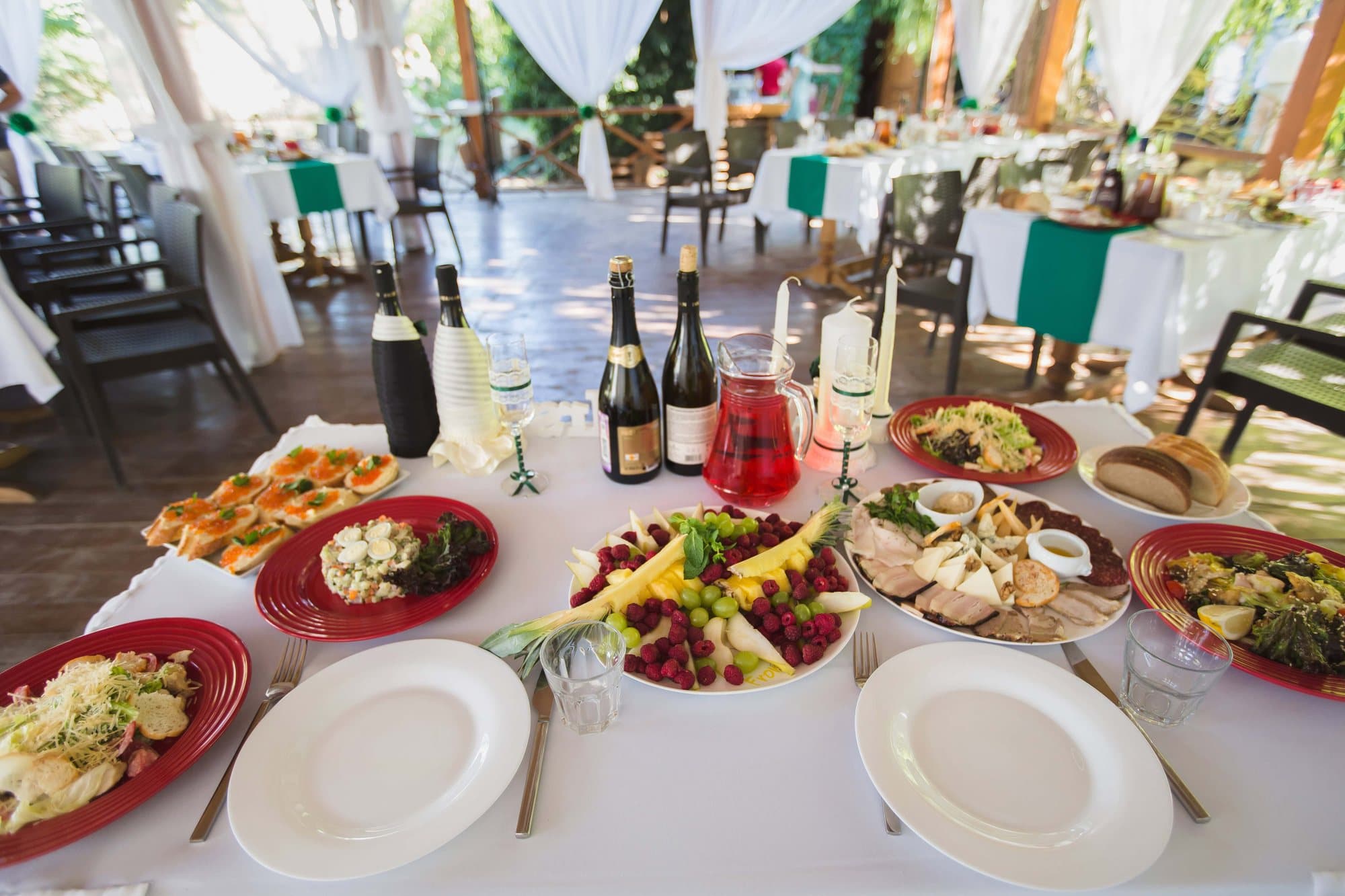 Mesa de banquete servida con entrantes, vino y copas en una carpa