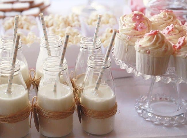Botellitas de leche con pajitas y cupcakes en una mesa dulce infantil