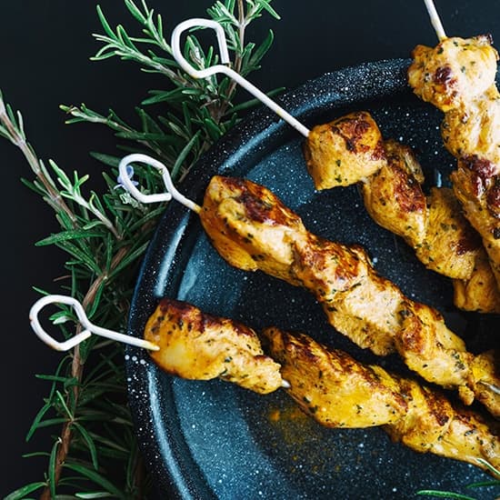 Brochetas de pollo marinado con romero sobre plato esmaltado
