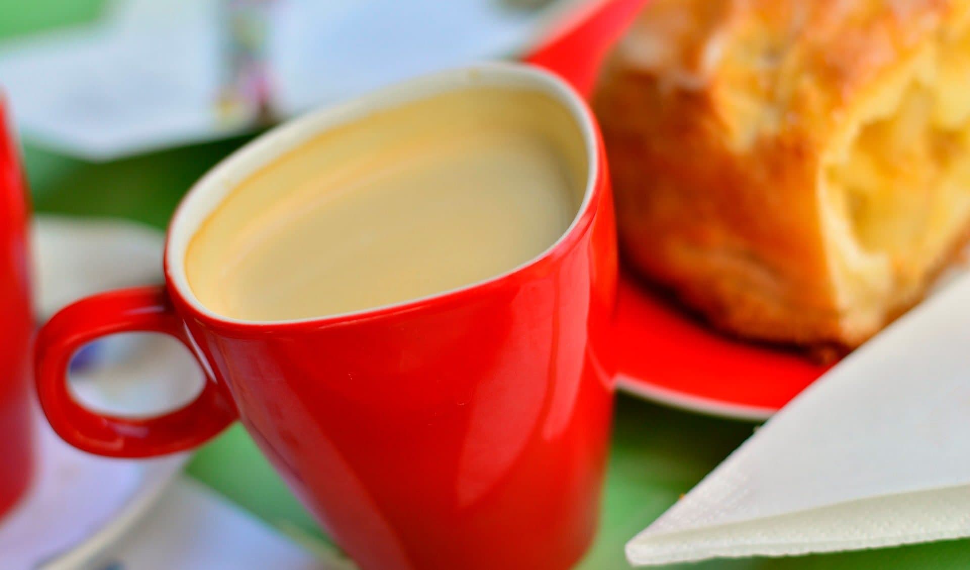 Café con leche en taza roja junto a bollería recién horneada del obrador