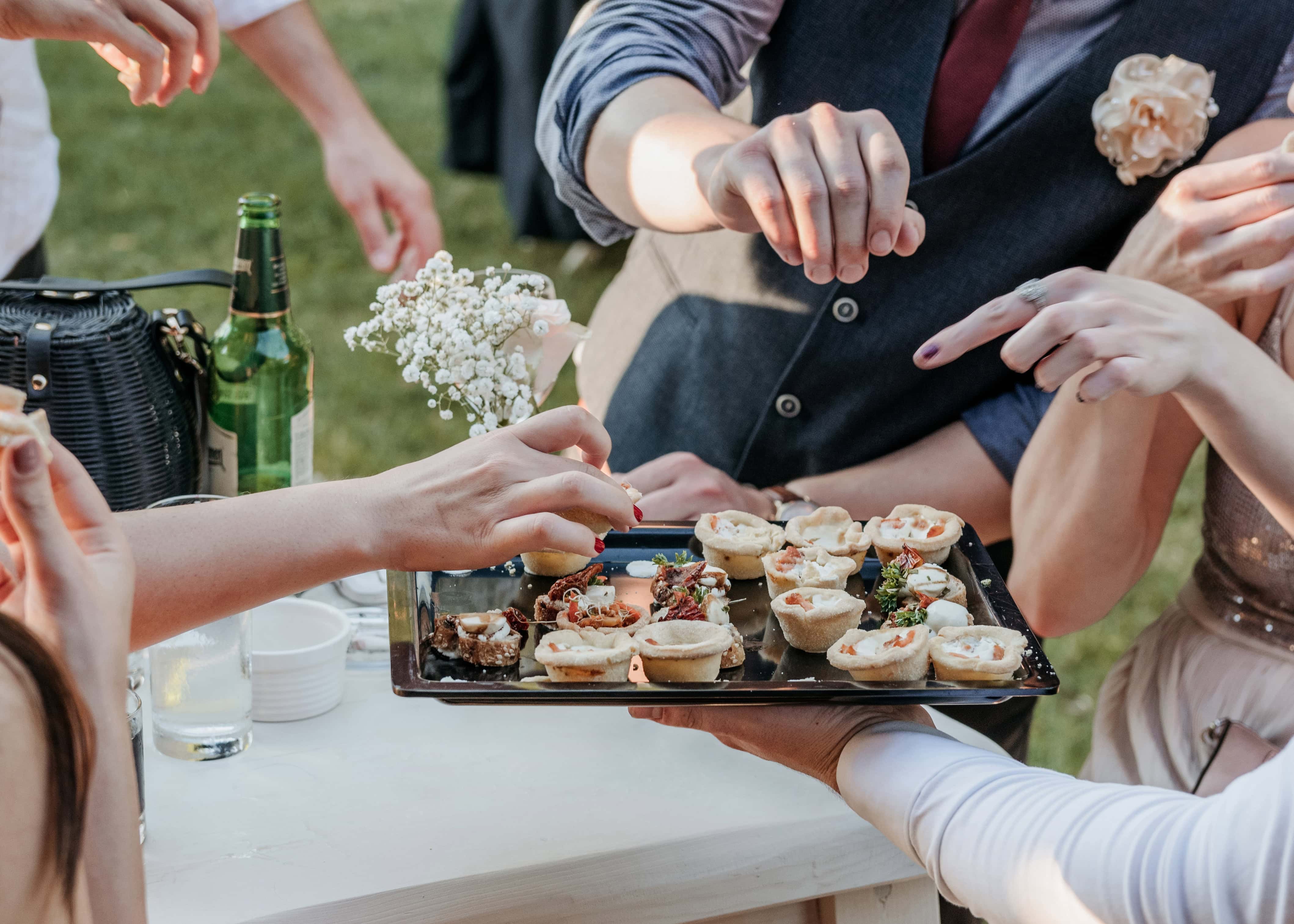 Invitados tomando canapés de una bandeja en una boda al aire libre