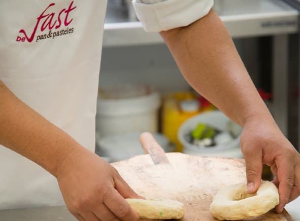 Manos de panadero formando roscas de masa con delantal de Fast
