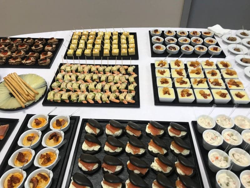 Mesa de buffet con bandejas de canapés variados y vasitos de crema
