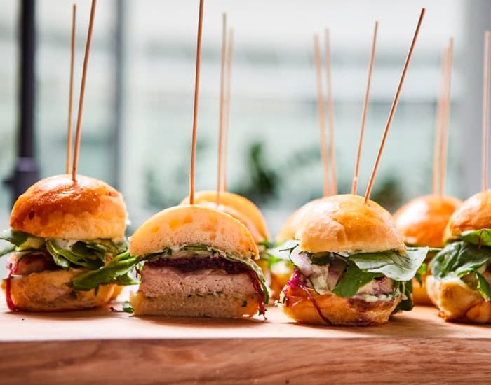 Mini hamburguesas de pollo con rúcula sobre tabla de madera