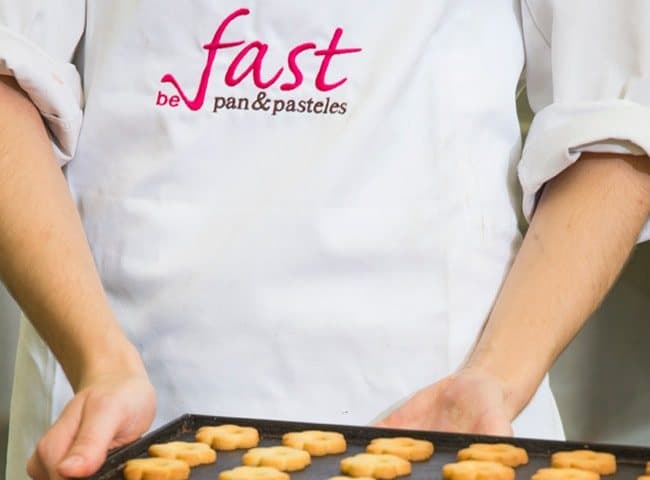Panadero con delantal de Fast sujetando una bandeja de galletas recién horneadas