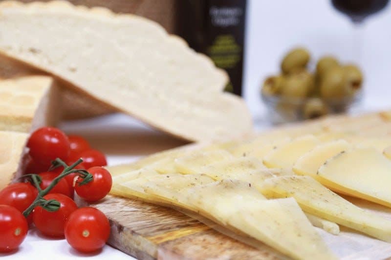 Tabla de queso curado laminado con pan, tomates cherry y aceitunas